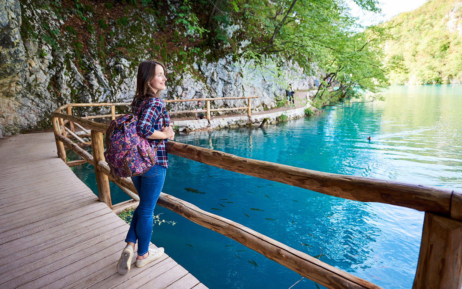 Guest walking along wooden path by turquoise lake at Plitvice Lakes National Park.