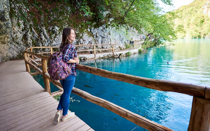 Guest walking along wooden path by turquoise lake at Plitvice Lakes National Park.