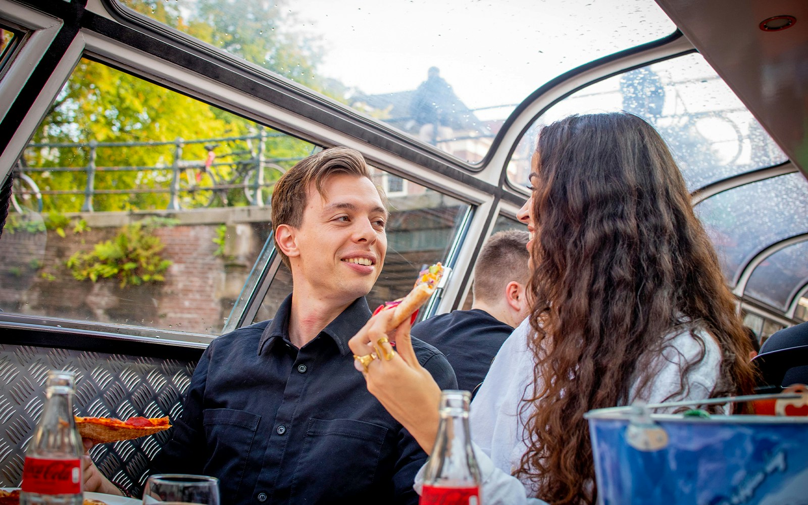 Amsterdam canal cruise with pizza and drinks, view of historic buildings and bridges.