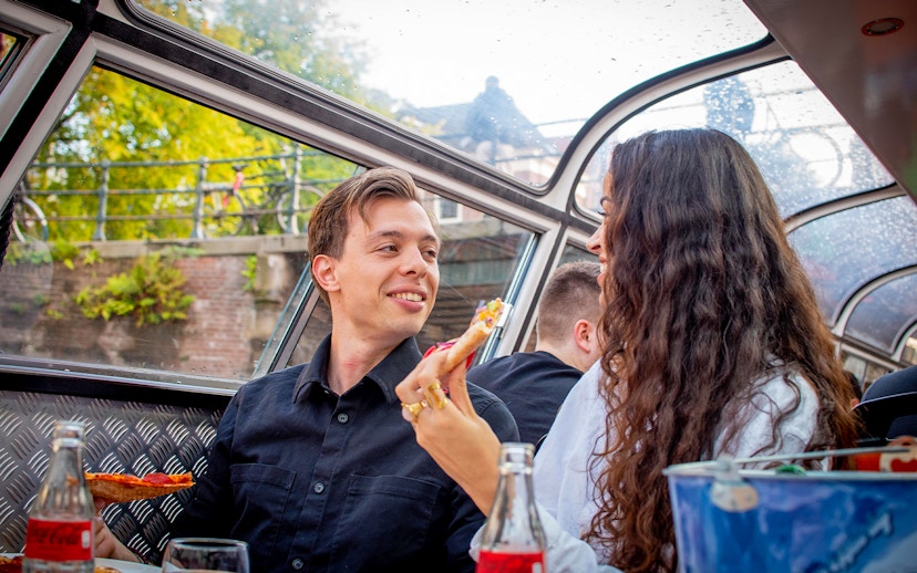 Couple enjoying pizza and drinks on an Amsterdam canal cruise.