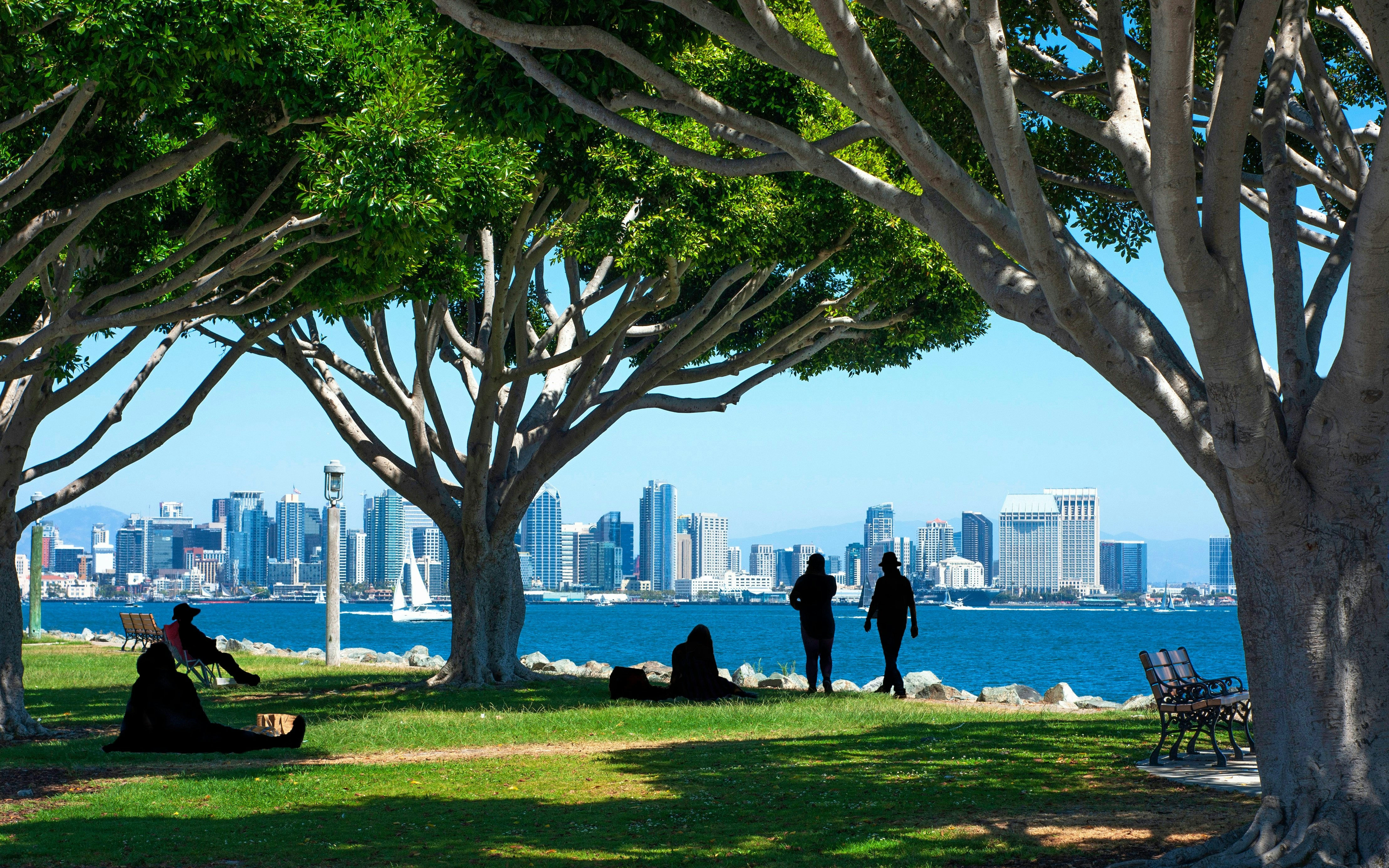 Silhouetted people at Spanish Landing Park with city skyline and bay in background.