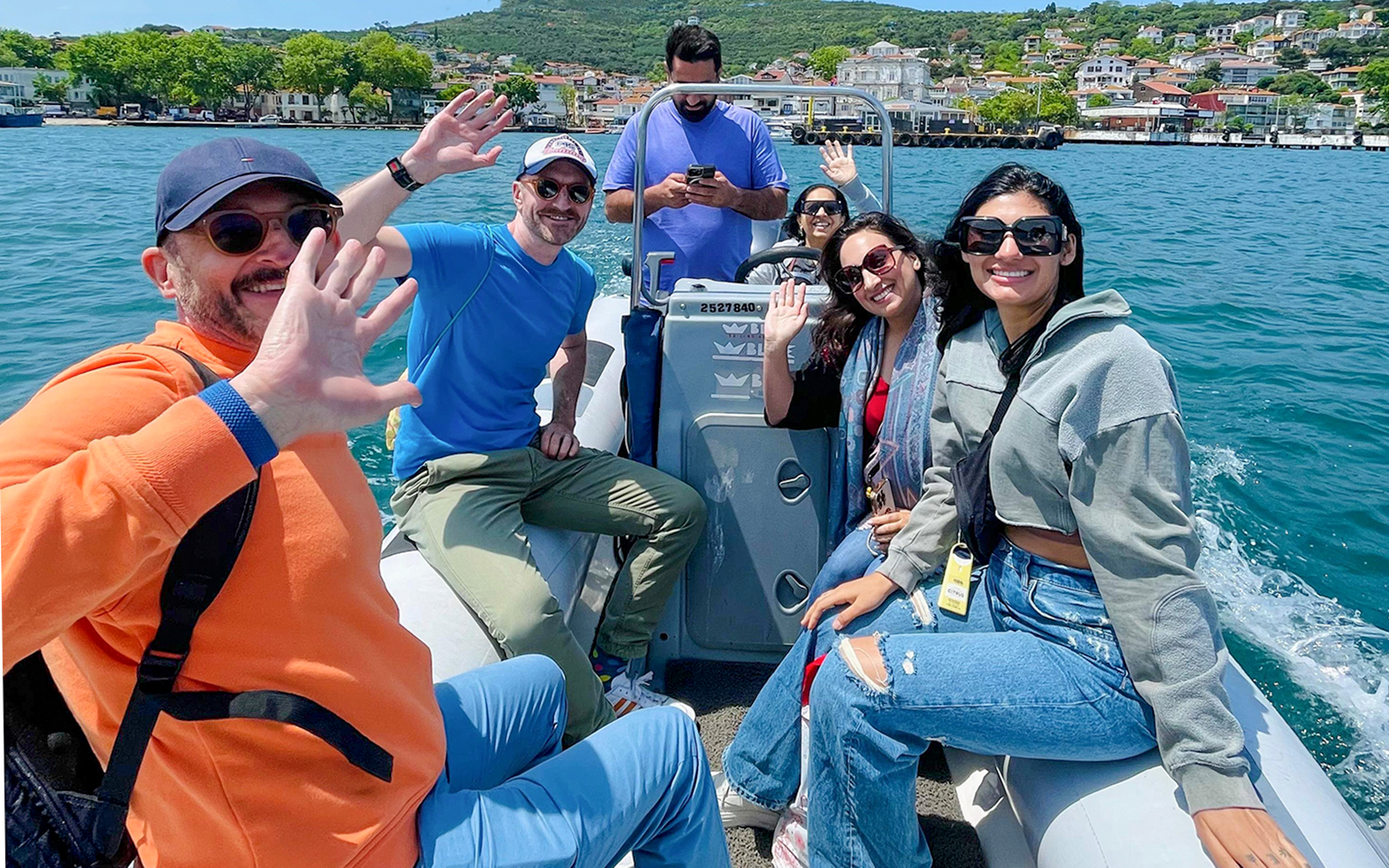 Guests waving during a speedboat ride near a coastal town.