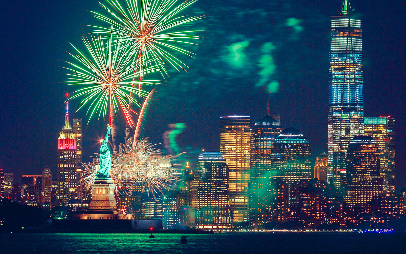 Fireworks over the Statue of Liberty and New York City skyline at night.