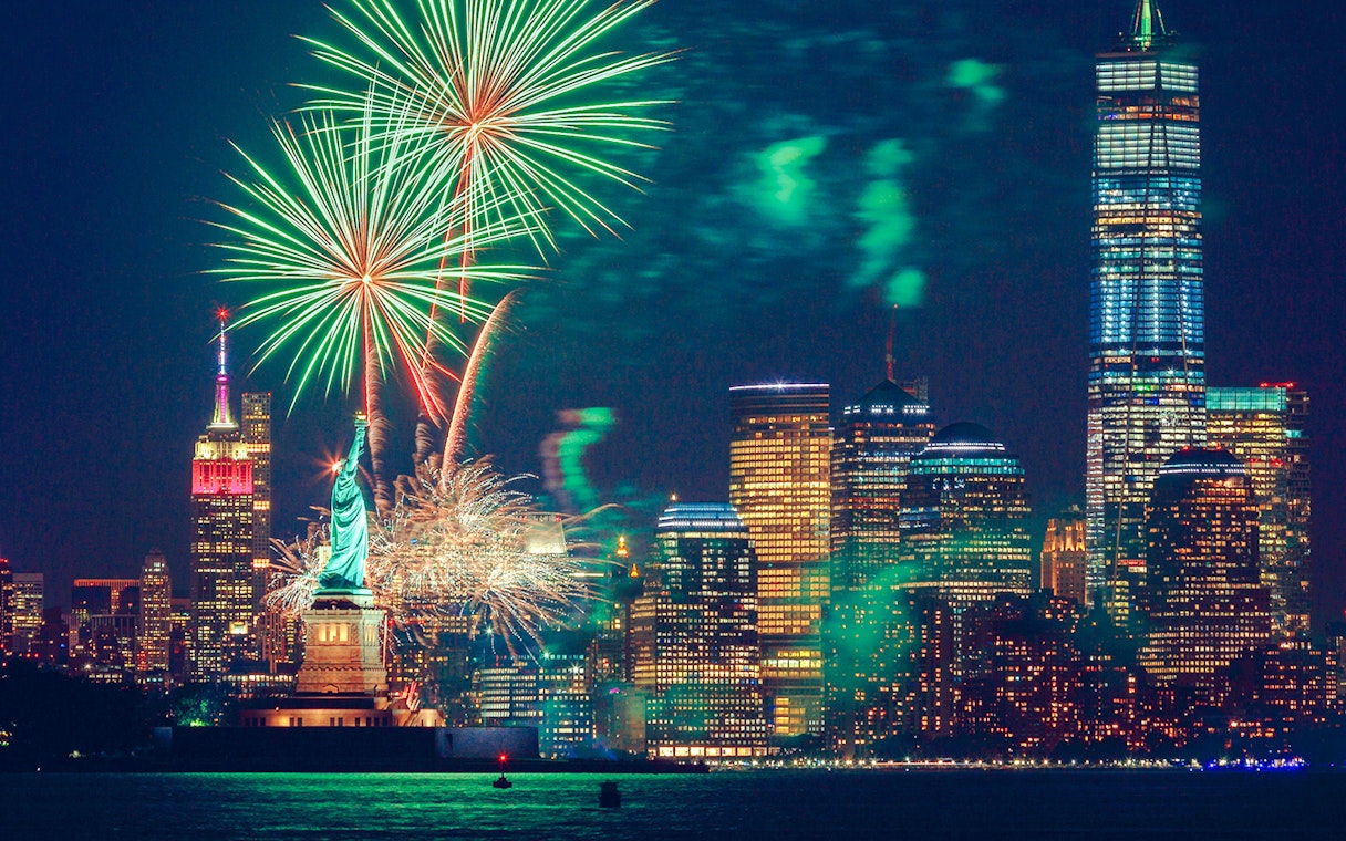 Fireworks over the Statue of Liberty and New York City skyline at night.