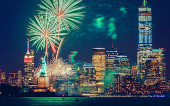 Fireworks over the Statue of Liberty and New York City skyline at night.