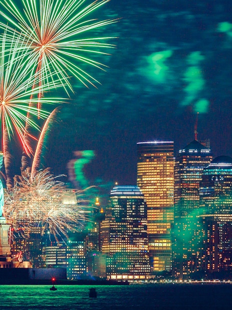 Fireworks over the Statue of Liberty and New York City skyline at night.