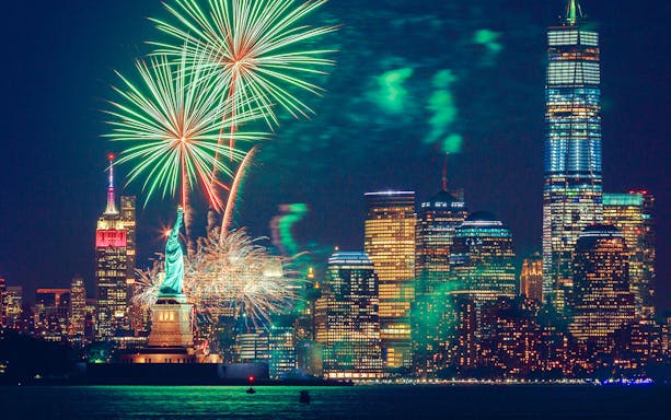 Fireworks over the Statue of Liberty and New York City skyline at night.