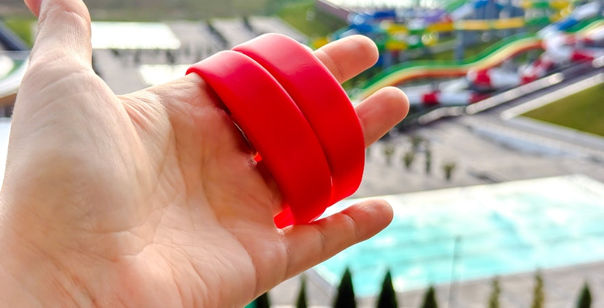 Red wristbands held in hand with colorful water park slides in the background.
