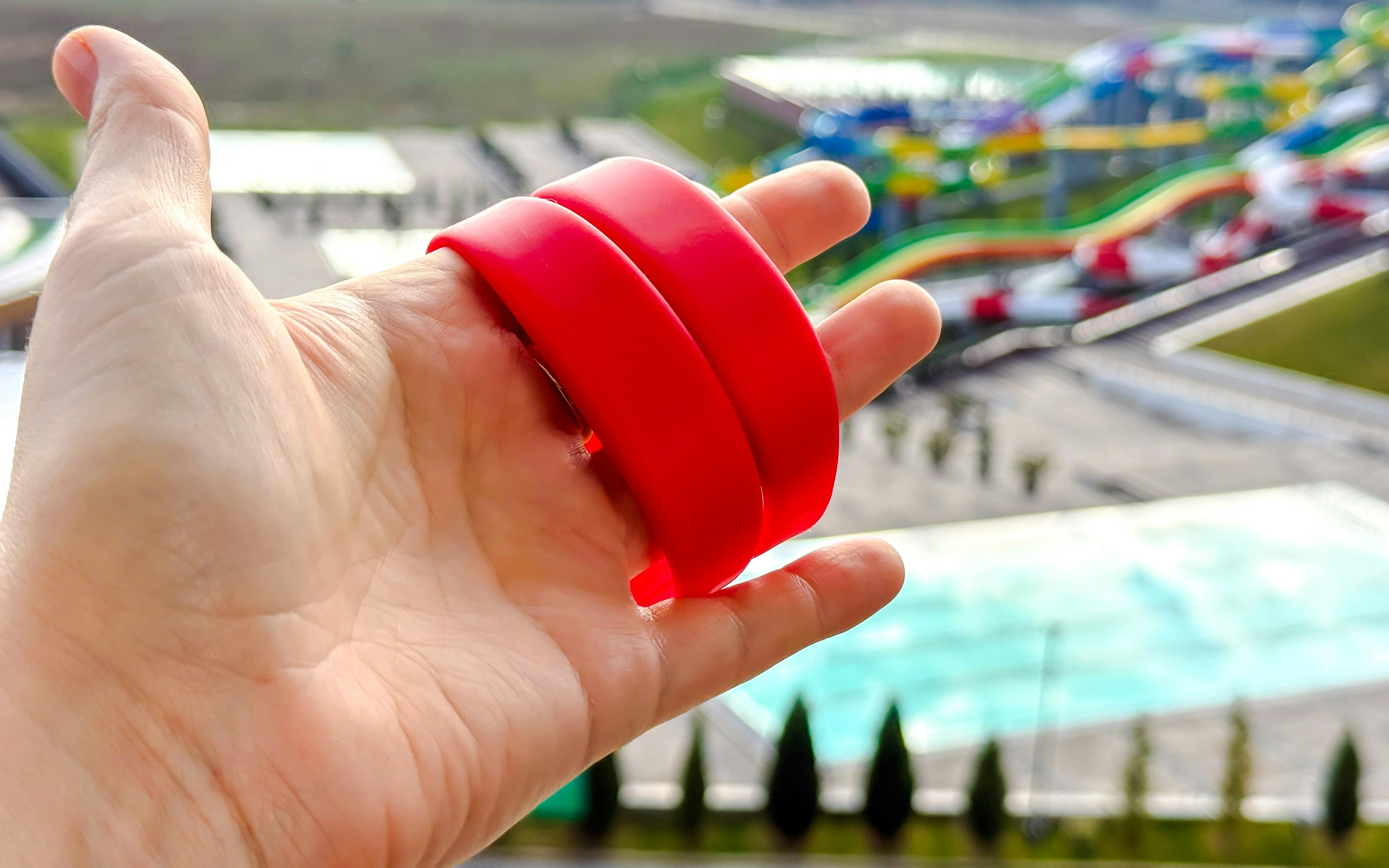 Red wristbands held in hand with colorful water park slides in the background.