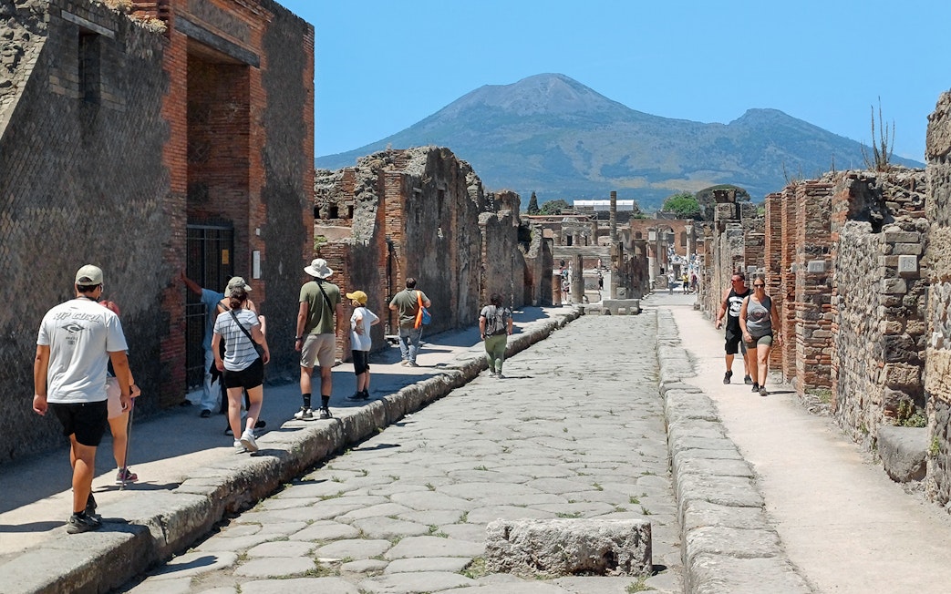 Visitors exploring ancient streets of Pompeii with Mount Vesuvius in the background.