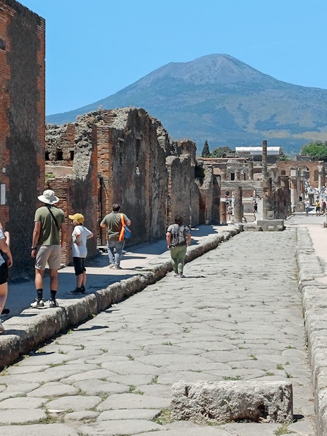 Visitors exploring ancient streets of Pompeii with Mount Vesuvius in the background.