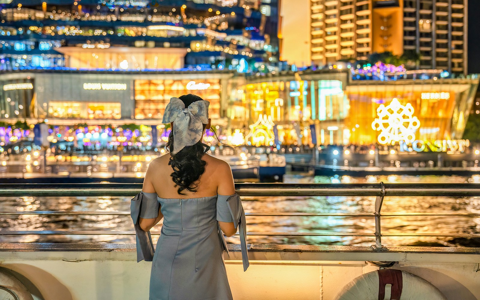 Lady looking at illuminated buildings from a cruise ship on the Chao Phraya river.