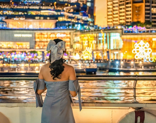 Lady viewing illuminated Bangkok buildings from a Chao Phraya river cruise ship.