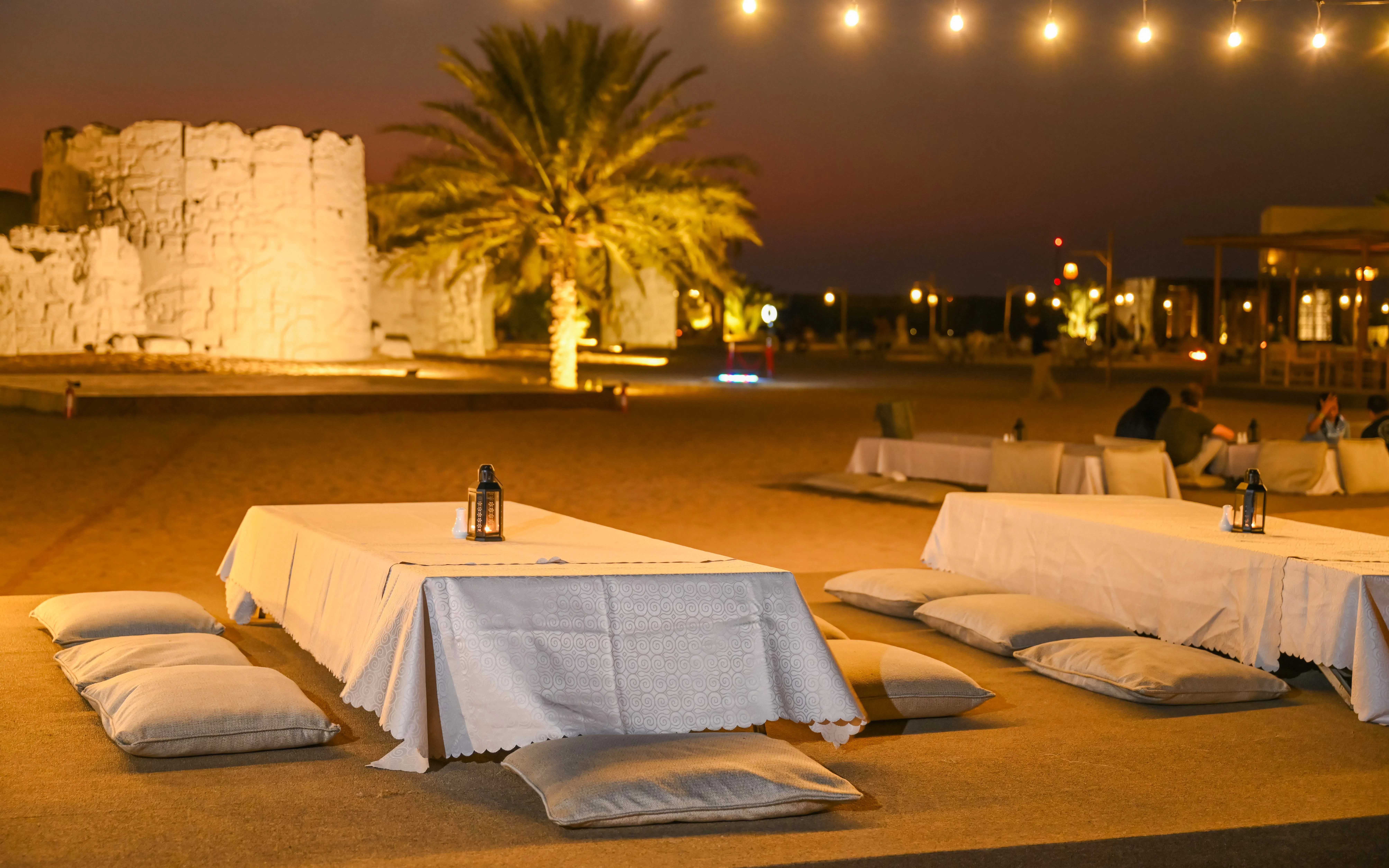 Dining setup at Dubai desert safari with cushions and lanterns under string lights.