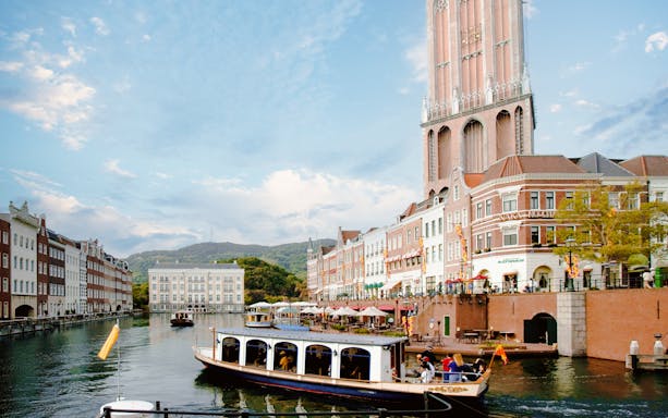 Canal boat tour at Huis Ten Bosch with European-style buildings and tower in Nagasaki, Japan.