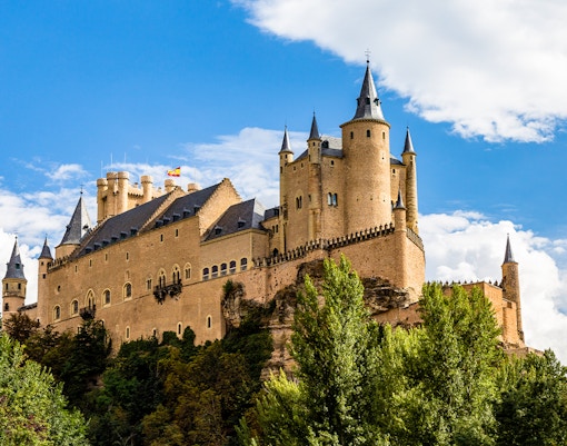 Alcazar of Segovia with towers and trees under a blue sky.