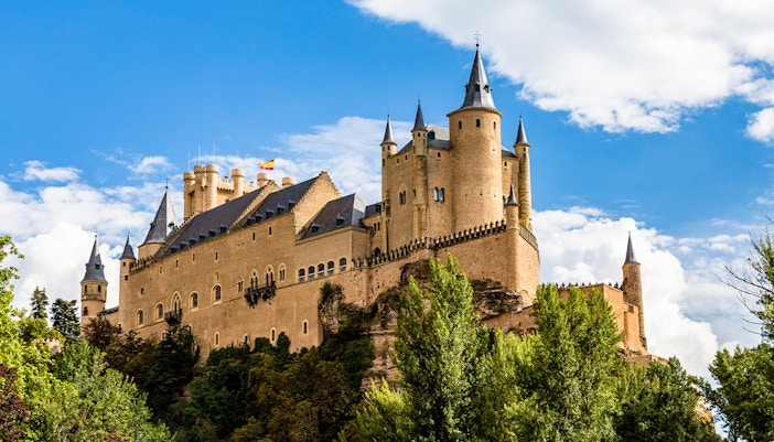 Alcazar of Segovia with towers and trees under a blue sky.