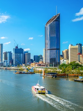 Brisbane river cruise boat passing city skyline with tall buildings.