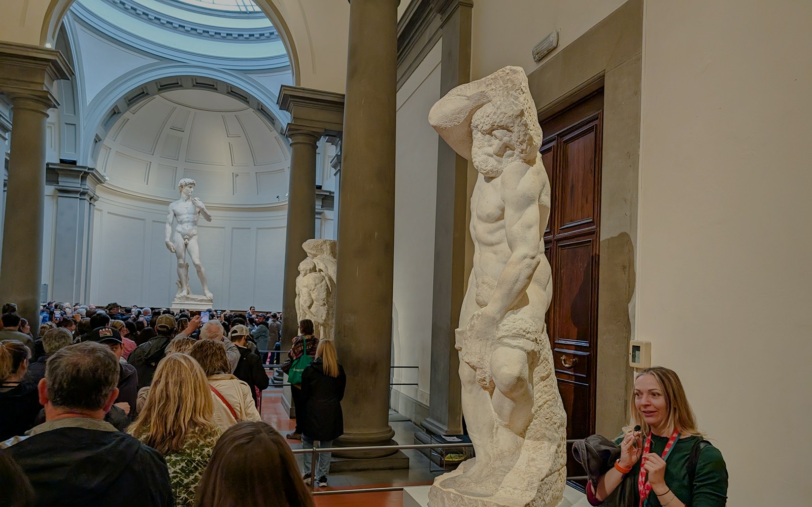 Bearded Slave sculpture in Accademia Gallery, Florence, with visitors nearby.