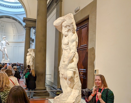 Bearded Slave sculpture in Accademia Gallery, Florence, with visitors nearby.