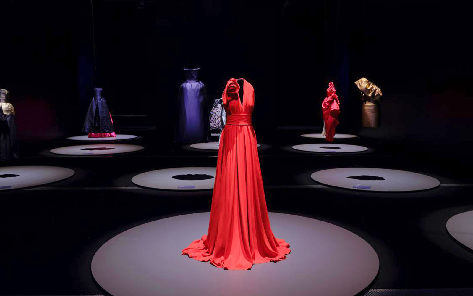 Red gown displayed at Martin Grant Exhibition with other fashion pieces in the background.