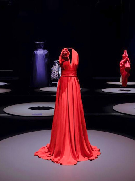 Red gown displayed at Martin Grant Exhibition with other fashion pieces in the background.