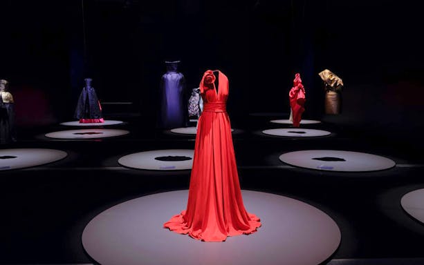 Red gown displayed at Martin Grant Exhibition with other fashion pieces in the background.