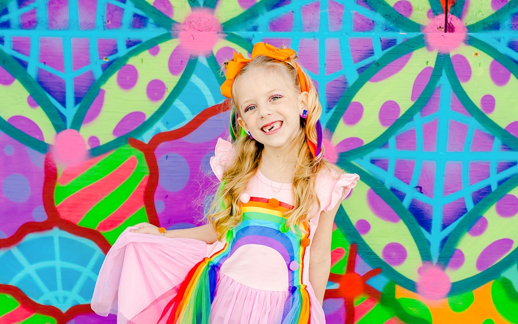 Girl smiling in front of a colorful geometric mural.