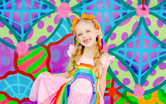 Girl smiling in front of a colorful geometric mural.