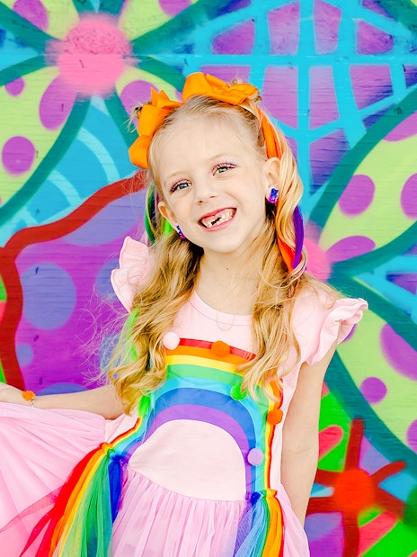Girl smiling in front of a colorful geometric mural.
