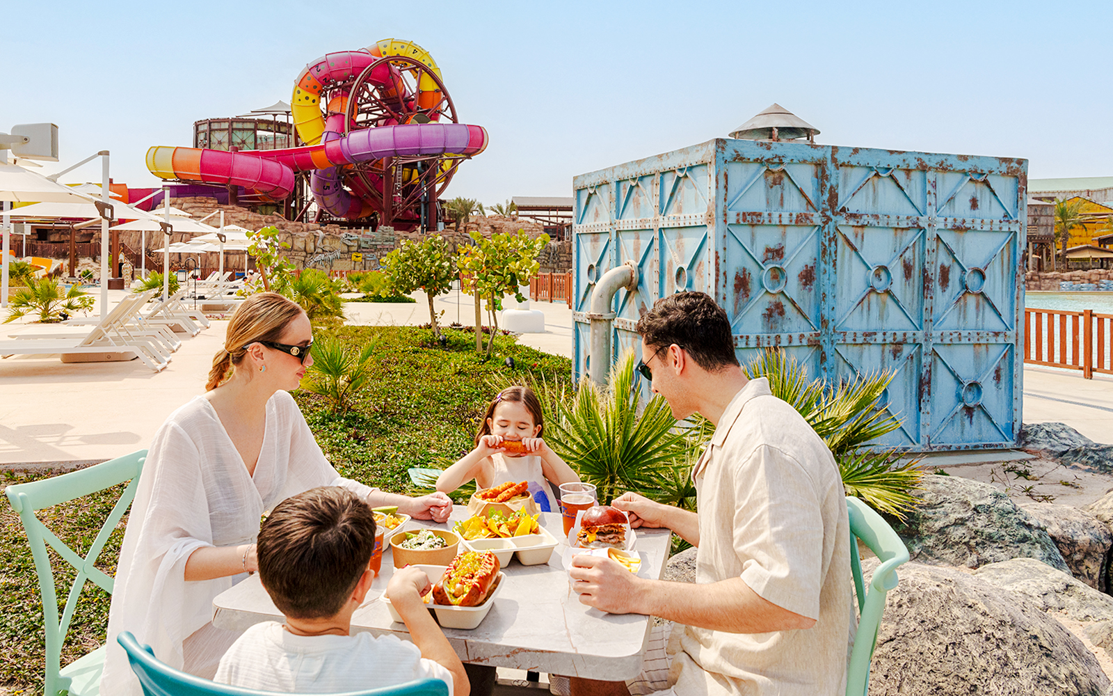 Family dining at Meryal Waterpark with colorful water slides in the background.