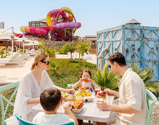 Family dining at Meryal Waterpark with colorful water slides in the background.