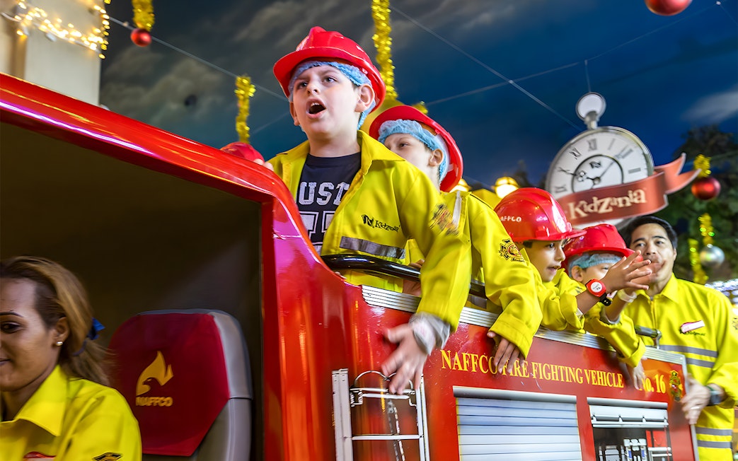 Kids in firefighter uniforms on a fire truck at Kidzania Abu Dhabi.