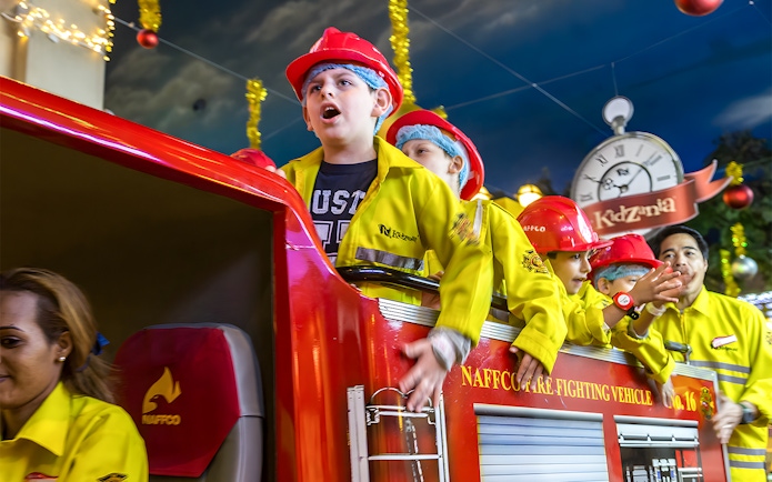 Kids in firefighter uniforms on a fire truck at Kidzania Abu Dhabi.