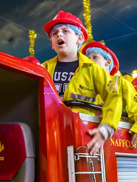 Kids in firefighter uniforms on a fire truck at Kidzania Abu Dhabi.