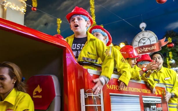 Kids in firefighter uniforms on a fire truck at Kidzania Abu Dhabi.