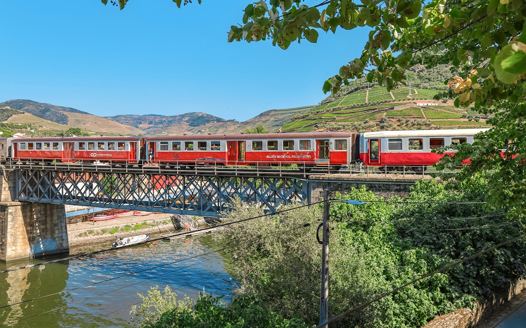 Train crossing a bridge in Douro Valley, Portugal, with vineyards in the background.