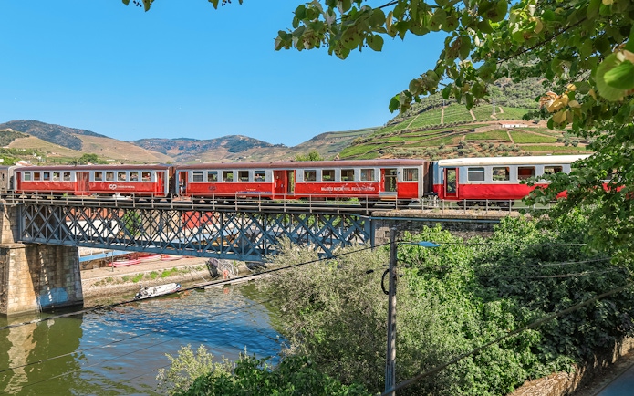 Train crossing a bridge in Douro Valley, Portugal, with vineyards in the background.