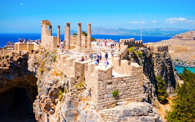 Tourists exploring the ancient ruins of the Acropolis of Lindos in Greece with sea views.