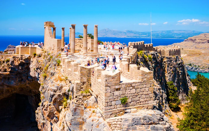 Tourists exploring the ancient ruins of the Acropolis of Lindos in Greece with sea views.