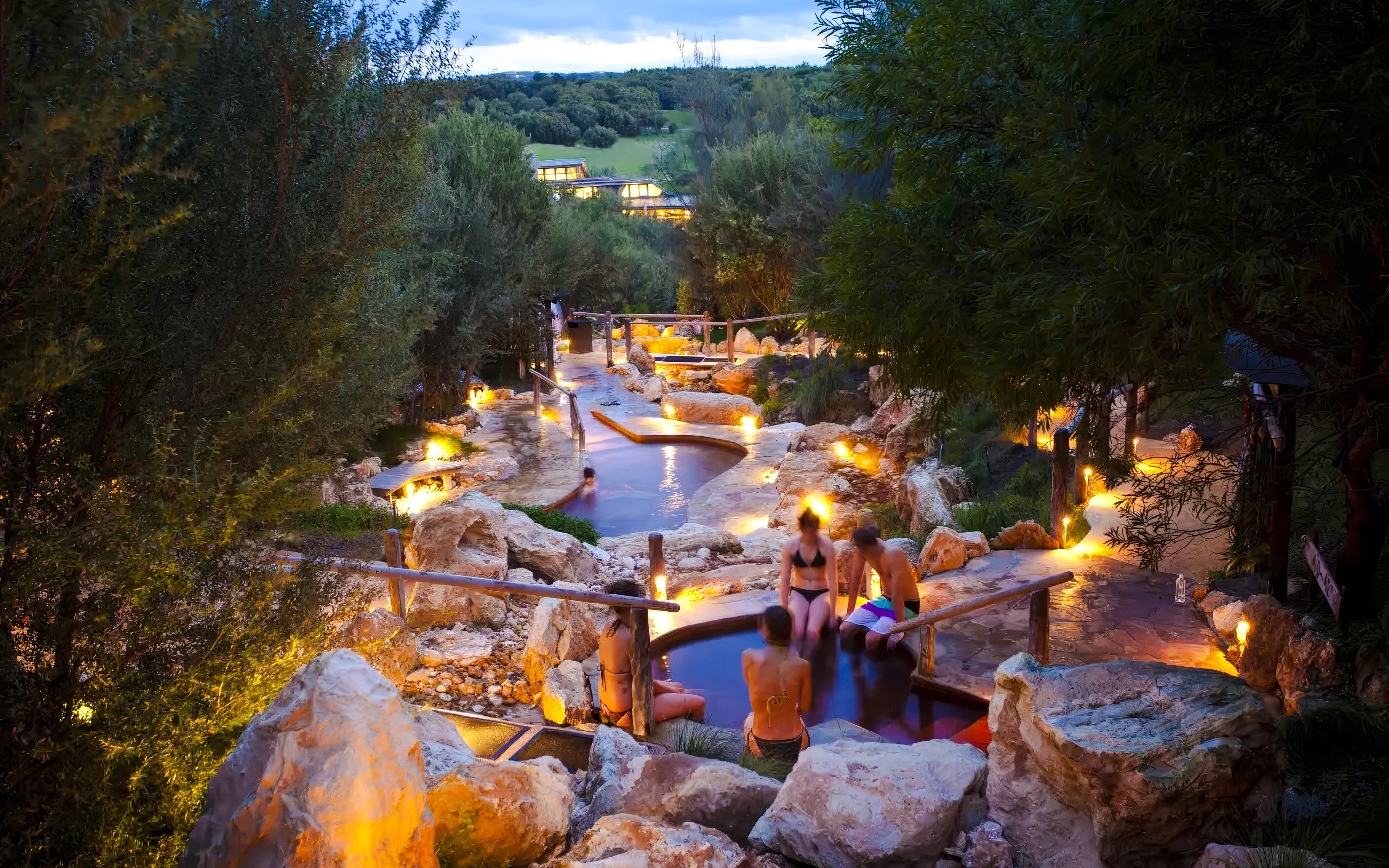 Visitors relaxing in geothermal pools at Peninsula Hot Springs, surrounded by natural rock formations.