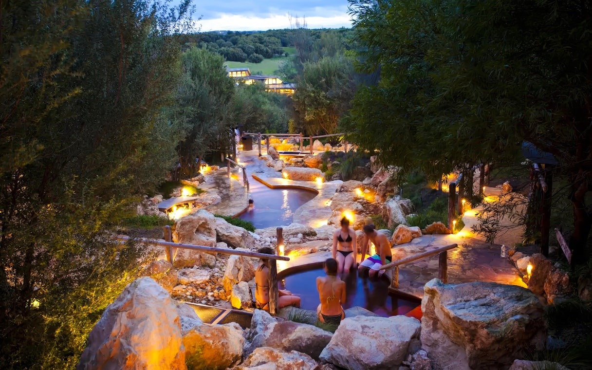 Visitors relaxing in geothermal pools at Peninsula Hot Springs, surrounded by natural rock formations.