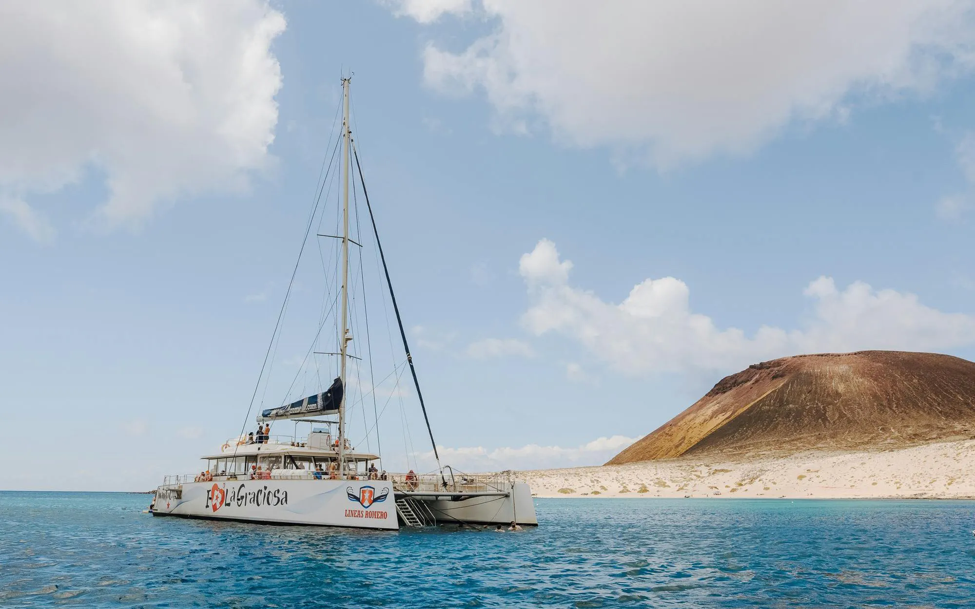 Catamaran sailing near La Graciosa Island with volcanic landscape in the background.
