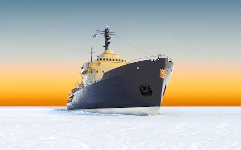 Icebreaker Sampo cruising through frozen sea at sunrise in Finland.