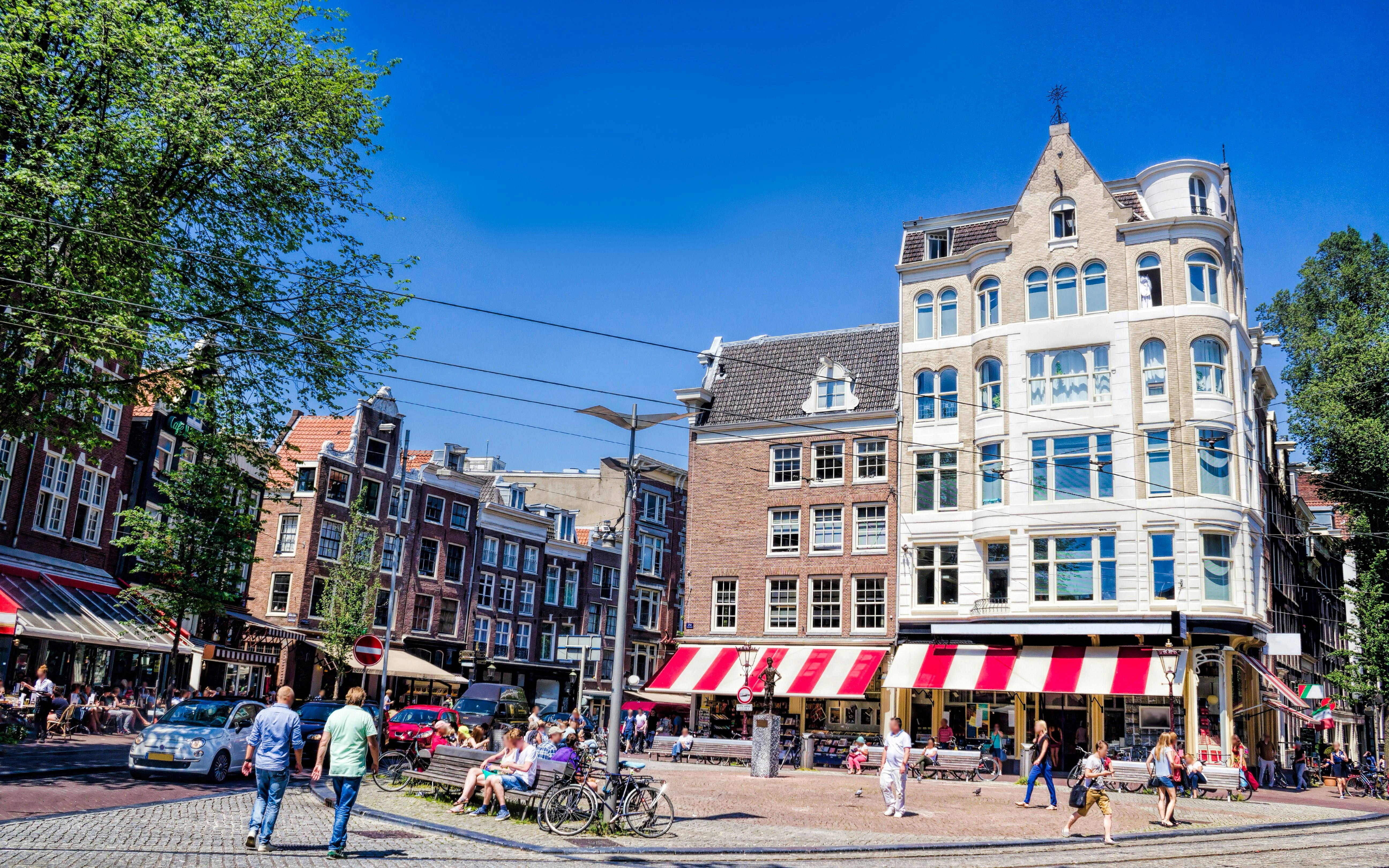 People walking and sitting at The Spui in Amsterdam, surrounded by historic buildings and cafes.