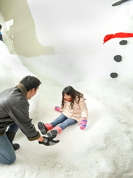 Child playing in snow with adult at Singapore Snow City.