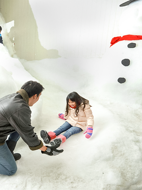 Child playing in snow with adult at Singapore Snow City.