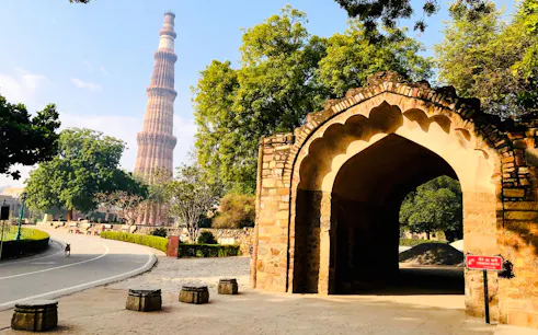 Qutub Minar and arched gateway surrounded by trees in Delhi.