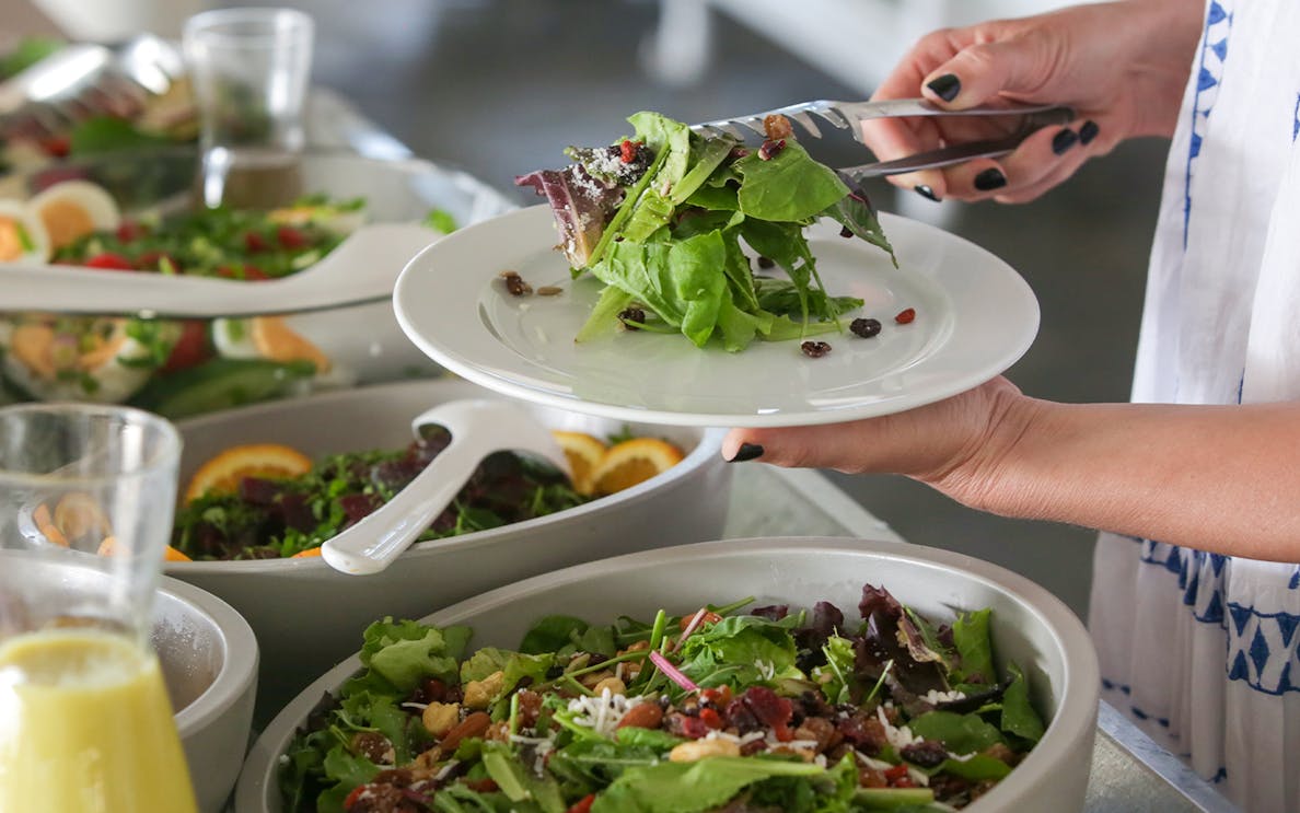 Woman serving salad from a buffet with various greens and toppings.