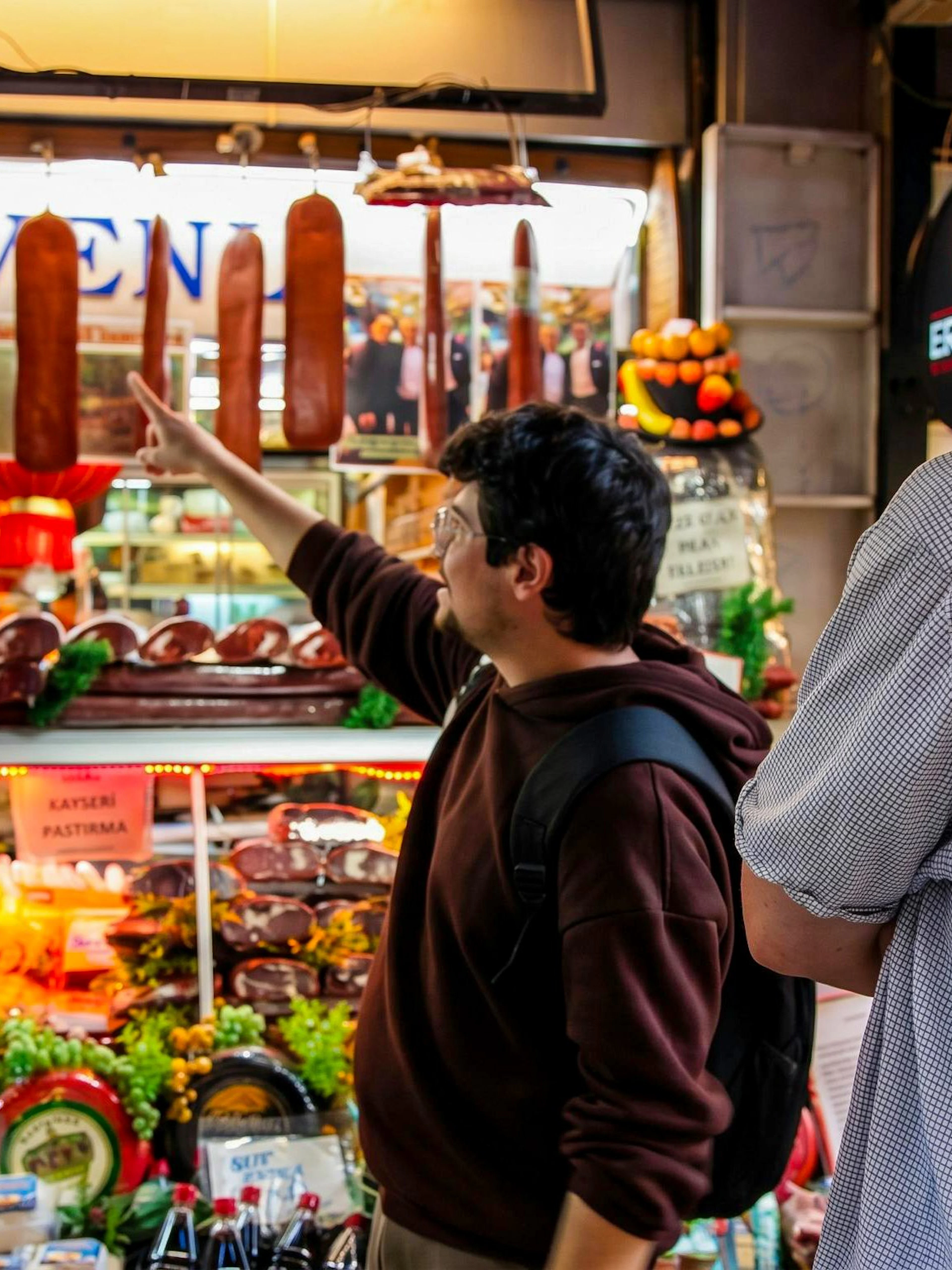 Tourists exploring a deli with hanging sausages on an Istanbul food tour.